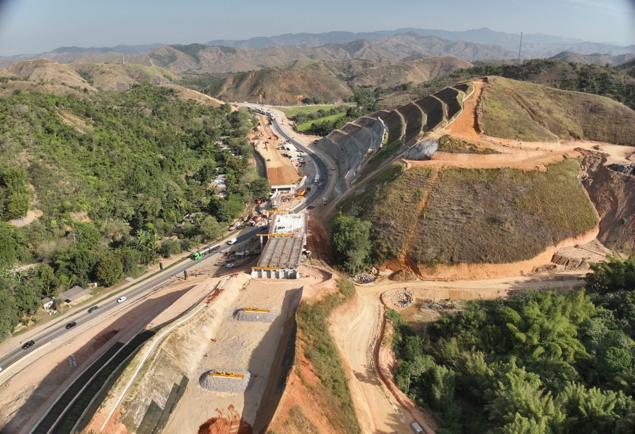 Vista aérea de viaduto em construção e corte em rocha na Nova Serra das Araras, com a Via Dutra ao fundo